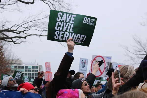 AFSCME member holds a sign above a crowd that says "Save Civil Service"